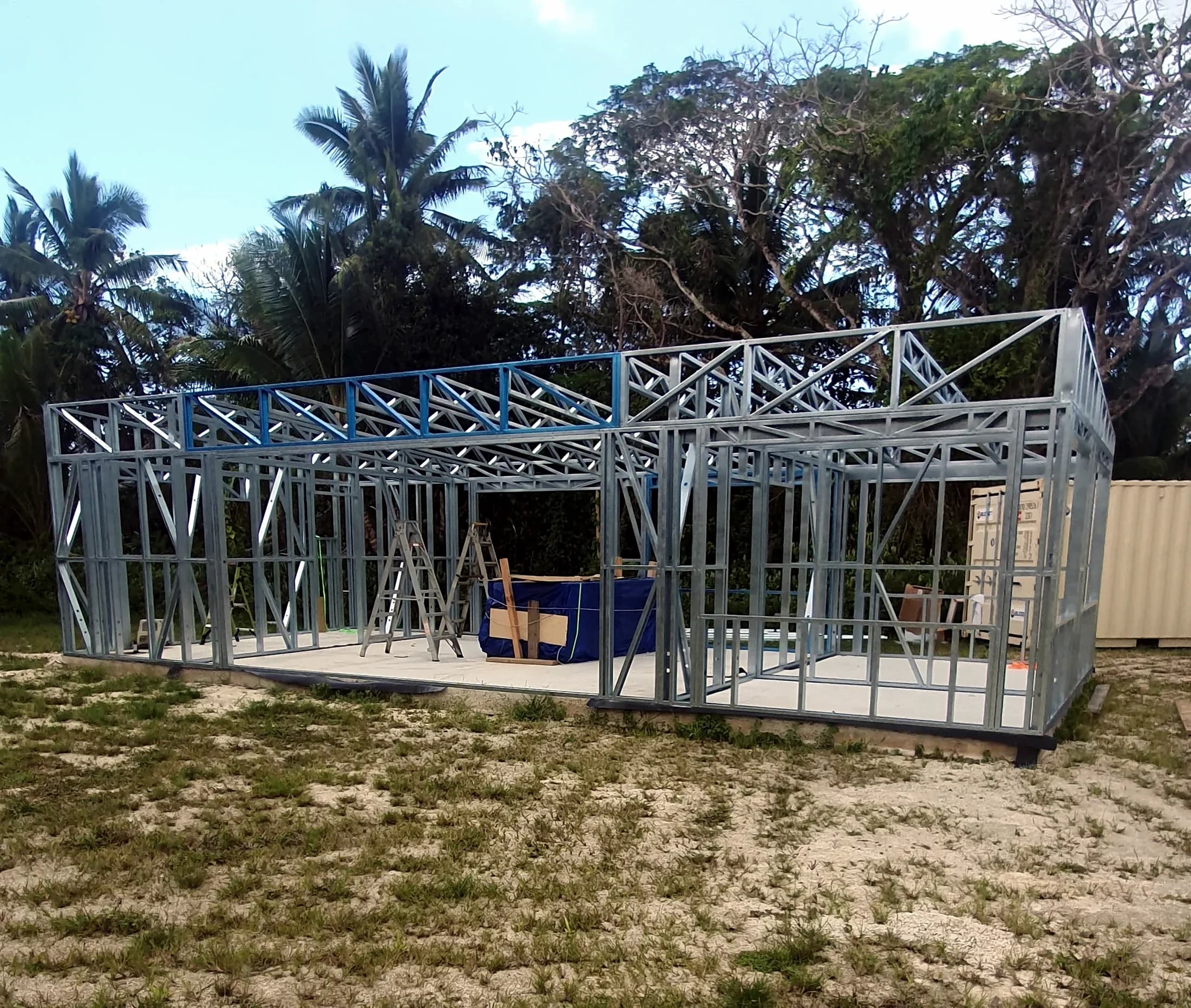 Light gauge steel wall frames and roof trusses standing on a slab, surrounded by palms